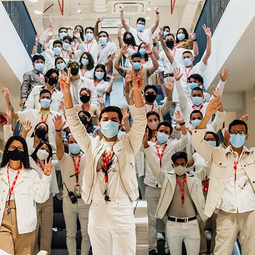 A large group of store employees wearing masks waving at the camera