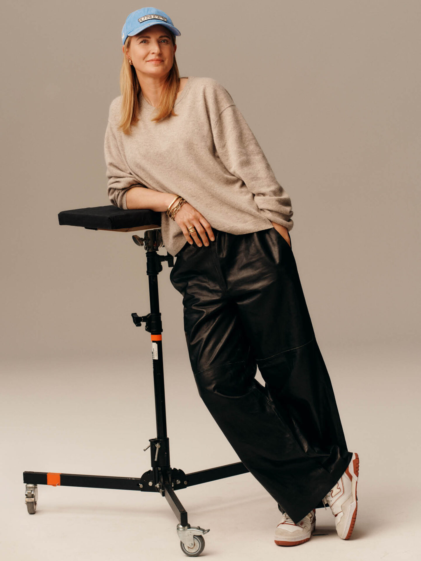 Communications expert leaning against a stool, wearing leader pants and a blue cap.