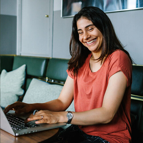 Млада служителка се усмихва, докато работи на лаптопа си