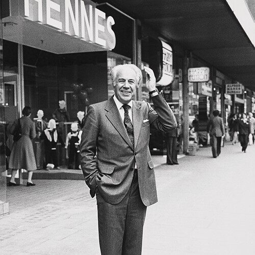 Černobílá fotografie muže stojícího před obchodem.