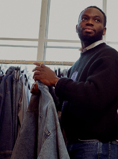 A male standing in front of a rail of clothes. Holding a few items of clothing, looking off camera.